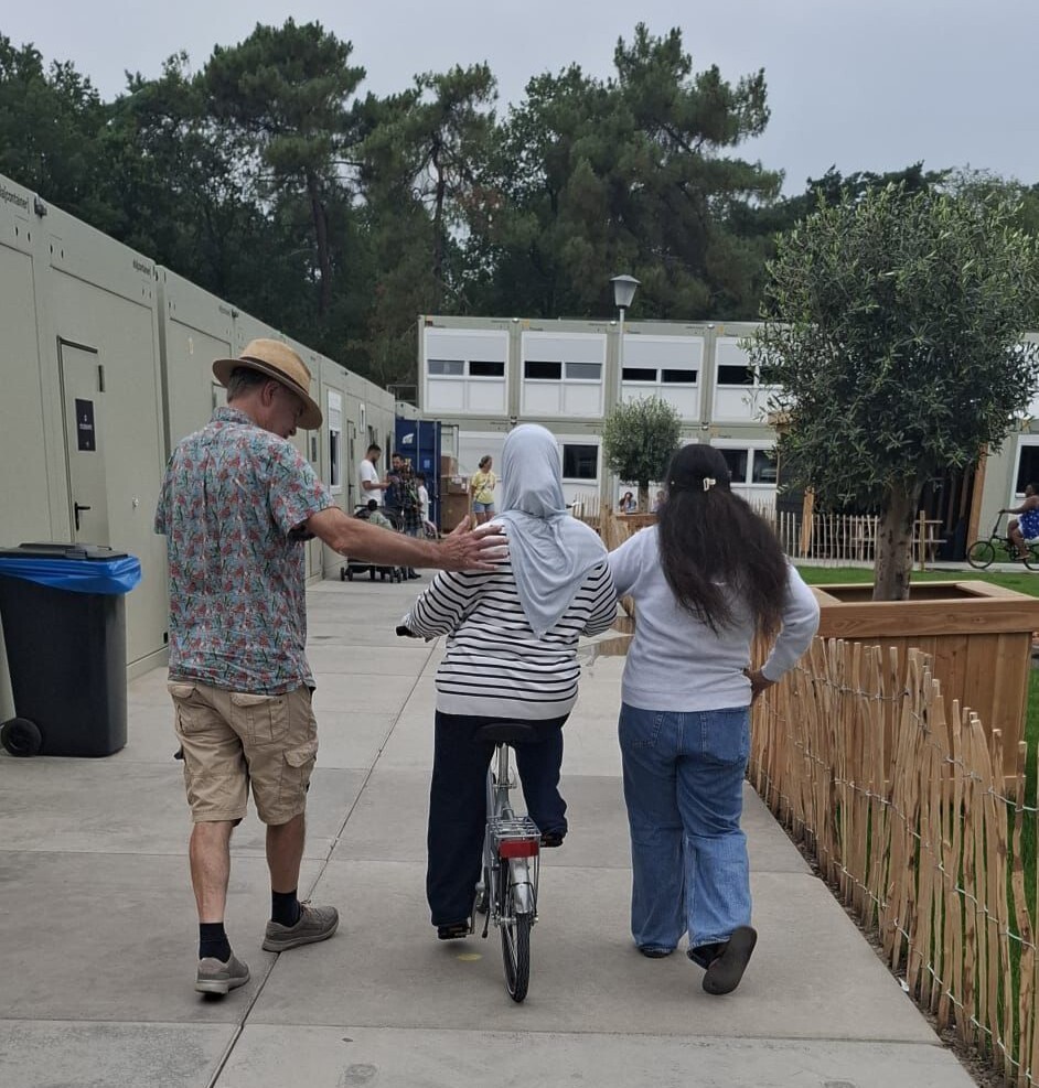 Vrijwilliger helpt een asielzoeker met het leren fietsen in de opvanglocatie.